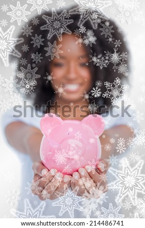 Pink piggy bank held by a woman in front of the camera against snowflakes on silver
