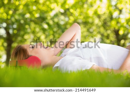 Pretty redhead lying on grass listening to music on a sunny day