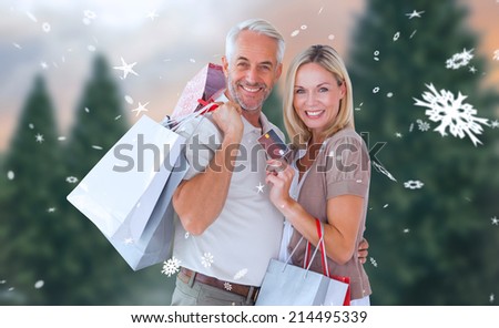 Happy couple with shopping bags and credit card against fir tree forest