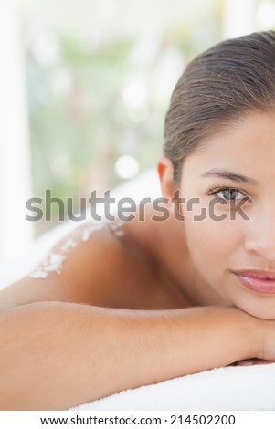 Beautiful brunette lying on massage table with salt scrub on back at the health spa