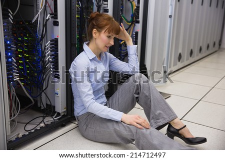 Stressed technician sitting on floor beside open server in large data center