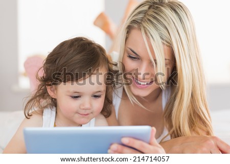 Mother and young daughter using digital tablet on bed at home