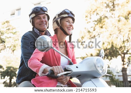 Happy senior couple riding a moped on a sunny day