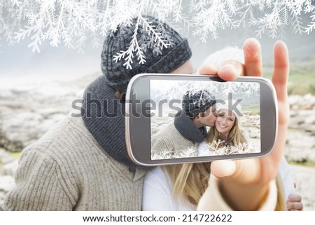 Hand holding smartphone showing man kissing a woman on rocky landscape
