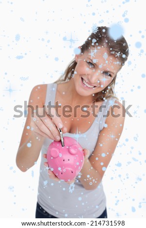 Portrait of a smiling woman putting a note in a piggy bank against snow falling