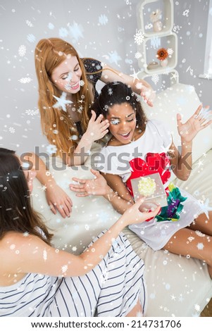 Cheerful young women surprising friend with a gift against snow falling