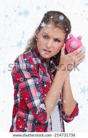Portrait of a sad woman shaking a piggy bank against snow falling