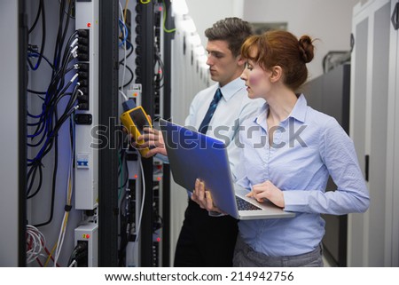 Team of technicians using digital cable analyser on servers in large data center