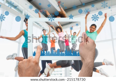 Hand holding tablet pc against fitness class and instructor jumping in fitness studio