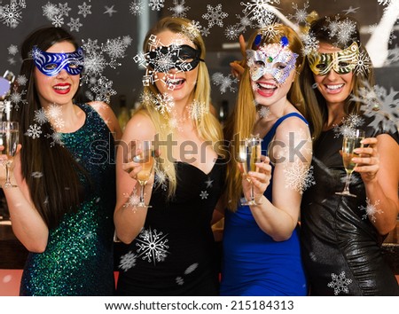 Laughing friends wearing masks holding champagne glasses against snowflakes
