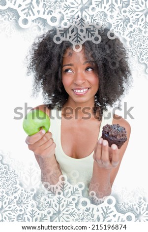 Young woman looking up to ask for help to choose between a fruit and chocolate against snowflakes on silver