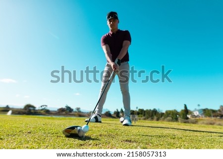 Low angle view of caucasian young man aiming ball with golf club while standing against clear sky. copy space, blue, summer, golf, unaltered, nature, sport and weekend activities concept. 商業照片 © 