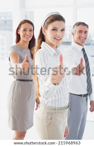 Smiling businesswoman giving thumbs up with co-workers