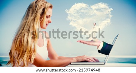 Composite image of pretty blonde using her laptop at the beach with heart cloud and hand