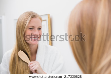 Happy blonde brushing her hair at home in the bathroom
