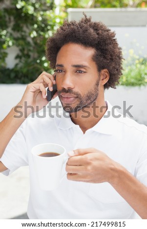 Smiling man on the phone having coffee outside at the coffee shop