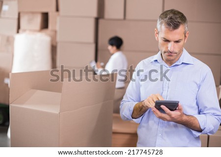 Warehouse manager using his calculator in a large warehouse