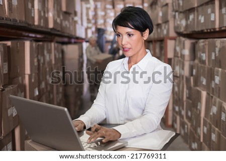 Pretty warehouse manager using laptop in a large warehouse