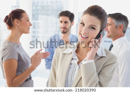 Businesswoman smiling while at work with co-workers while on phone