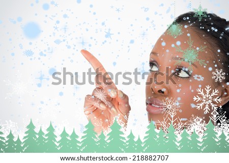 Close up of woman pointing at something next to her on a white background against snowflakes and fir trees in green