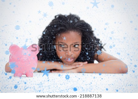 Young woman lying down resting her head on her hands is looking at a piggy bank against snow falling