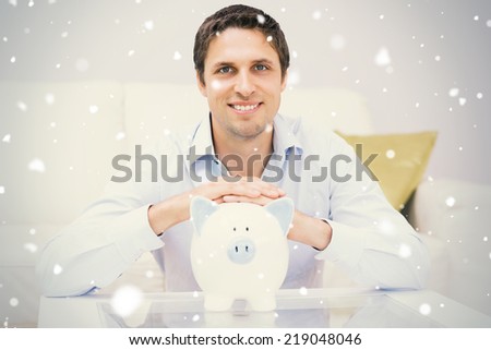 Handsome casual man with piggy bank in living room against snow falling