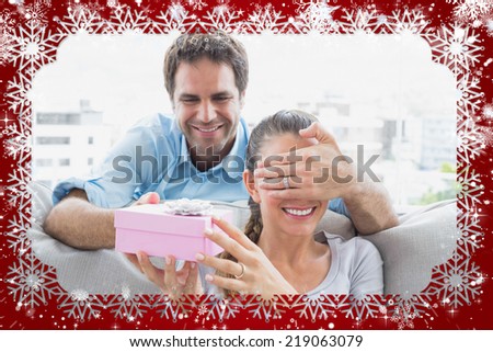 Man surprising his girlfriend with a pink gift on the sofa against snow