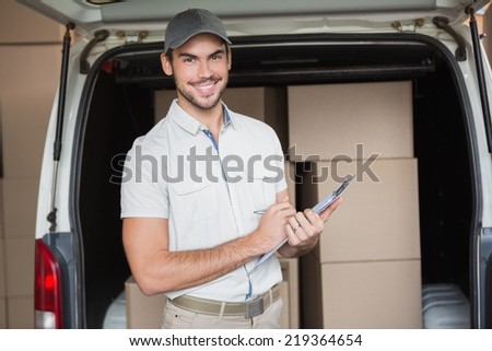 Delivery driver smiling at camera beside his van in a large warehouse