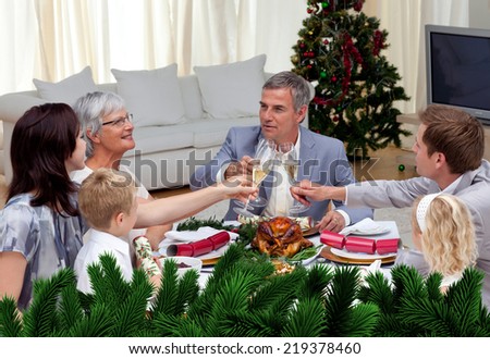 Family tusting in a Christmas dinner with champagne against digitally generated fir tree branches