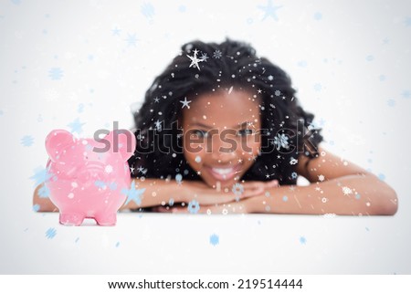 A smiling girl resting her head on her hands with a piggy bank in front of her against snow falling