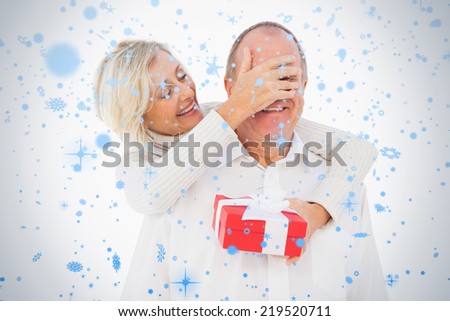 Older woman covering her partners eye while holding present against snow falling