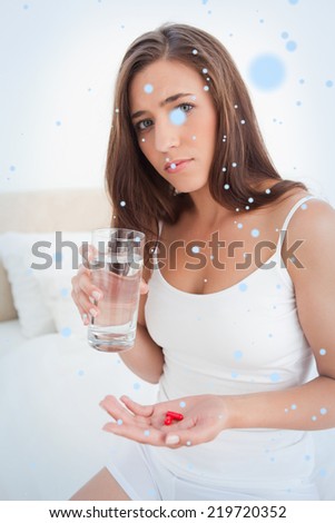 Woman looking worried as she is about to take two pills with water, against snow falling