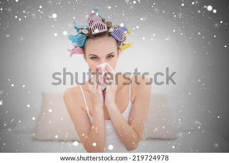 Cute natural brown haired woman in hair curlers sneezing in a tissue against snow