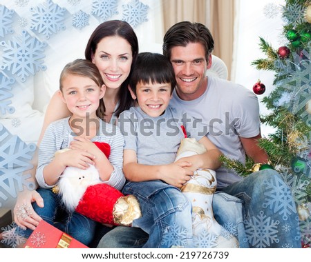 Portrait of a smiling family at Christmas time holding lots of presents against snowflake frame