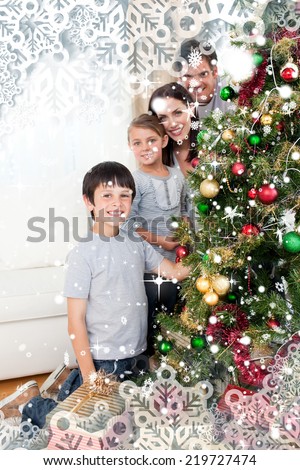 Happy family decorating a Christmas tree with boubles and presents against snow falling