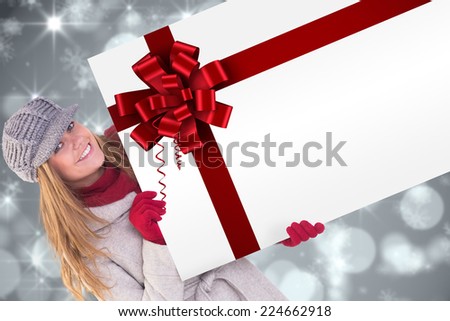 Happy blonde in winter clothes showing card against red christmas ribbon