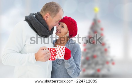 Mature couple holding mugs against blurry christmas tree in room