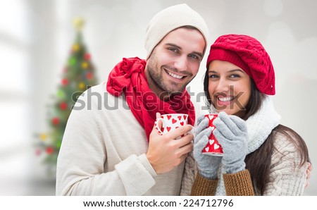 Winter couple holding mugs against blurry christmas tree in room