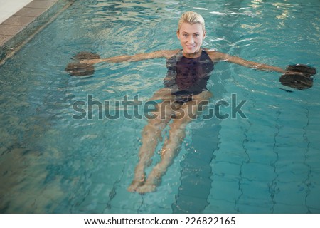 Portrait of a fit female swimmer working out with foam dumbbells in swimming pool at leisure centre