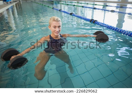 Portrait of a fit female swimmer working out with foam dumbbells in swimming pool at leisure centre