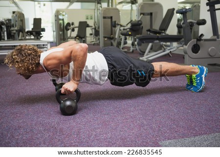 Side view of a handsome young man doing push ups with kettle bells in gym