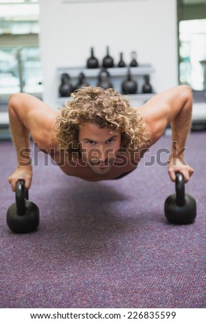 Portrait of a handsome young man doing push ups with kettle bells in gym