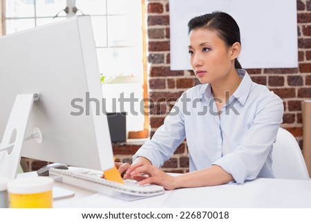 Concentrated young woman using computer at office desk