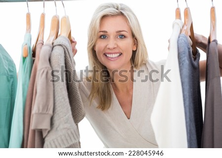 Pretty blonde smiling at camera by clothes rail on white background