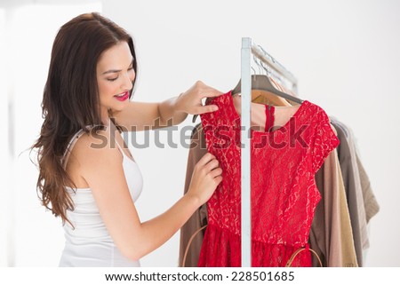 Pretty shopping brunette looking at red dress at clothes store