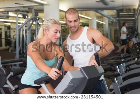 View of a male trainer assisting woman with exercise bike at the gym