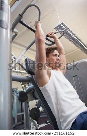 Fit man using weights machine for arms at the gym