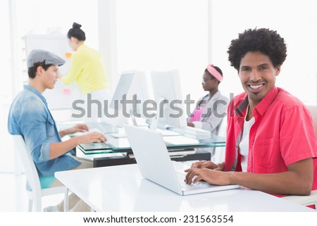 Young creative man using laptop at desk in creative office