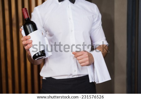 Handsome waiter holding a bottle of red wine and a towel in a bar