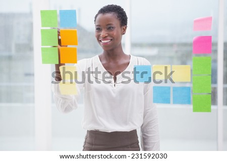 Smiling businesswoman writing on sticky notes on window in the office